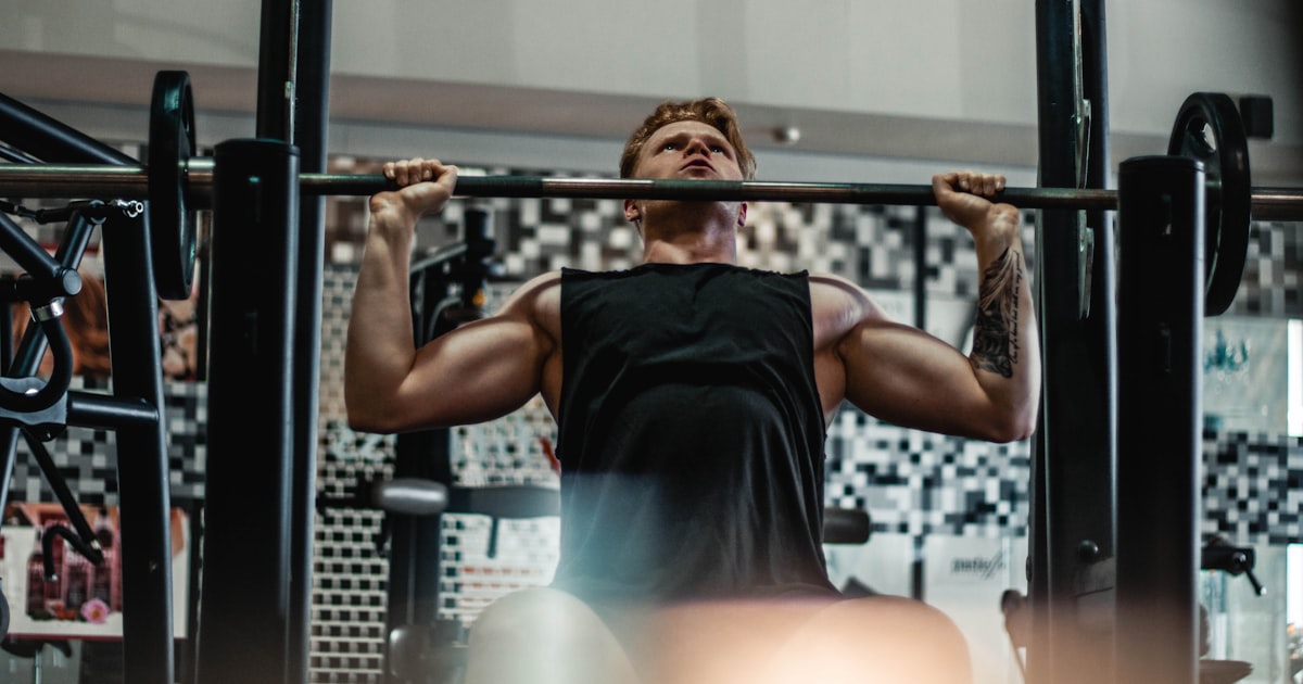 An athlete lifting a barbell with total focus, representing the discipline built by training consistently through summer